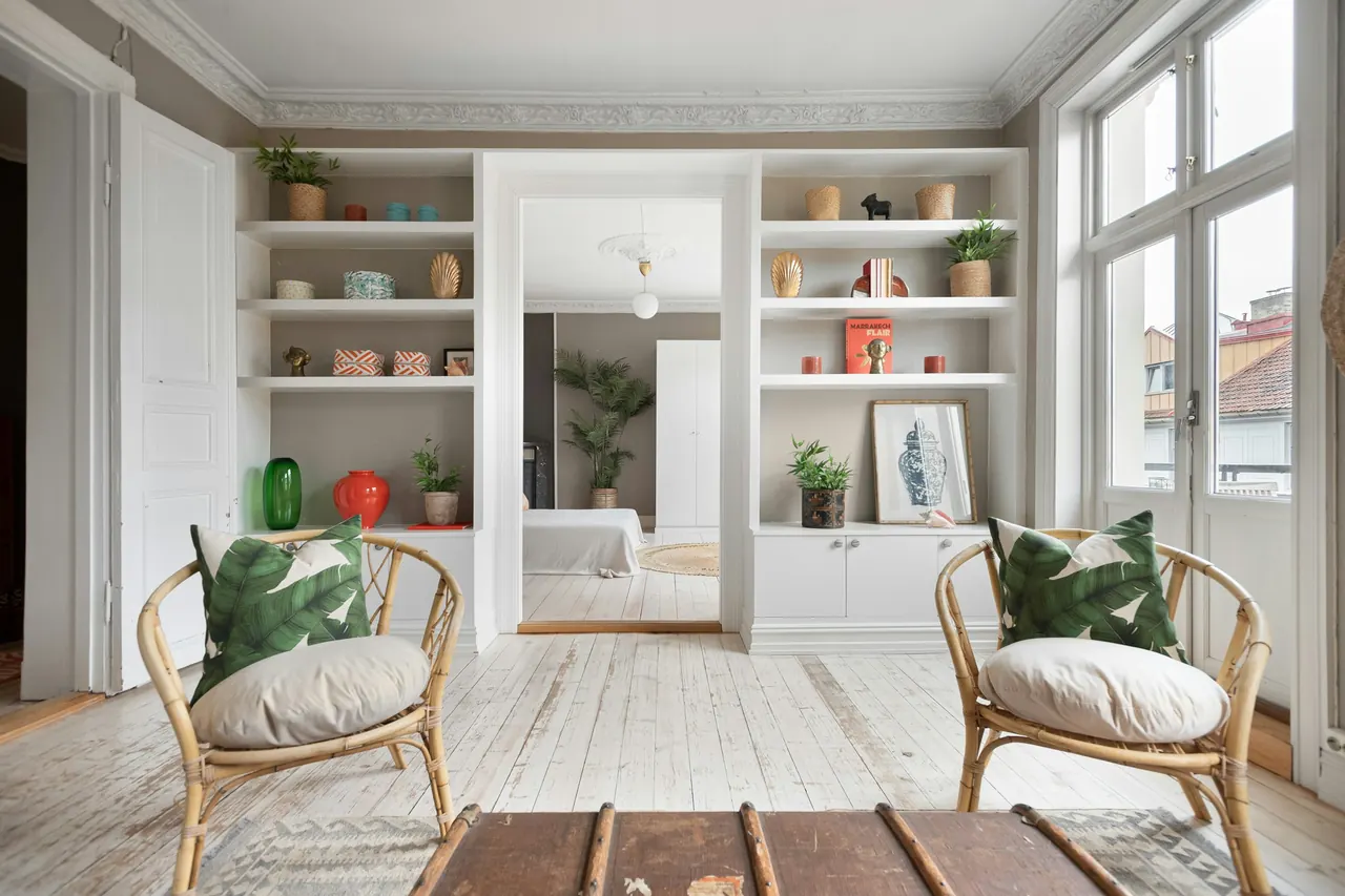 Salón con estanterías de obra, dos butacas de mimbre y grandes ventanas