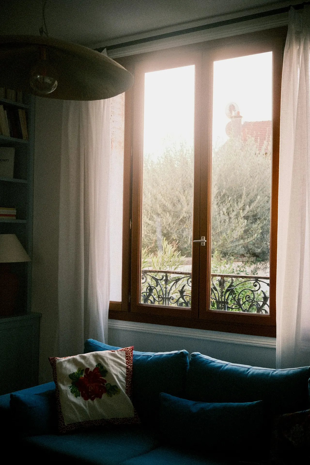 Ventana de madera abierta a la tarde, con un sofá azul debajo