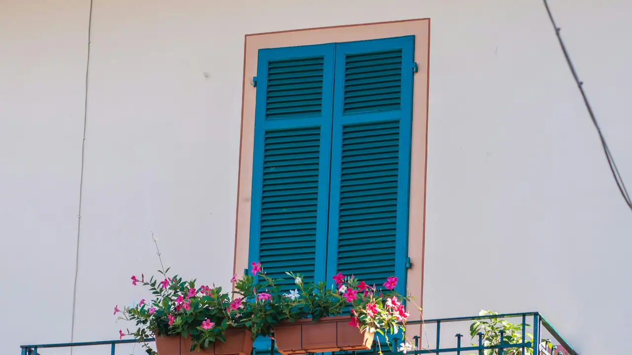 Balcón de forja con mallorquinas verdes y macetas con flores